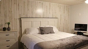 Een slaapkamer met een bed, nachtkastje, televisie en een dressoir.