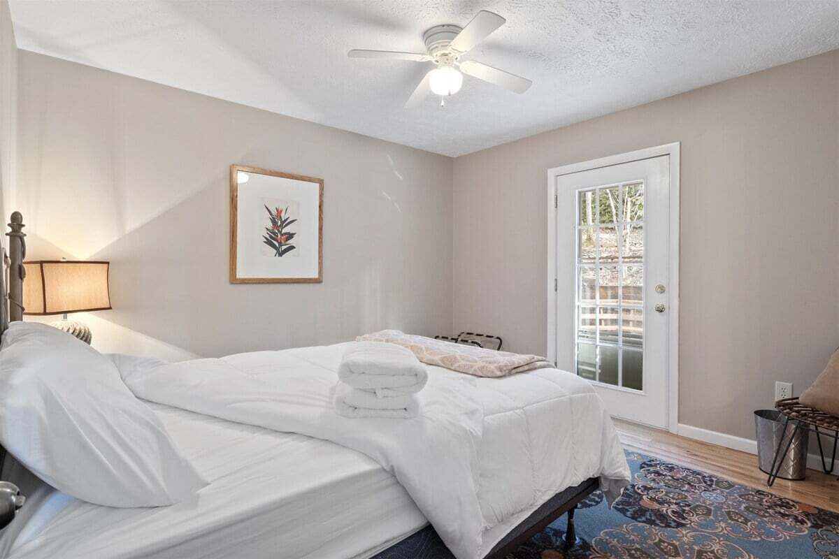 A bedroom with a bed, a ceiling fan, a door, and a window.