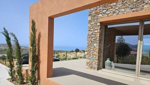 A modern building with a stone facade, a large glass door, and a view of the landscape. - EL-LU 2 Villa with breathtaking 360-degree seaview and a private pool (Kamilari)