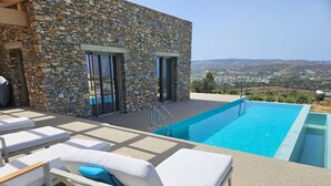 A poolside area with lounge chairs, a stone building, and a view of the landscape. - EL-LU 2 Villa with breathtaking 360-degree seaview and a private pool (Kamilari)