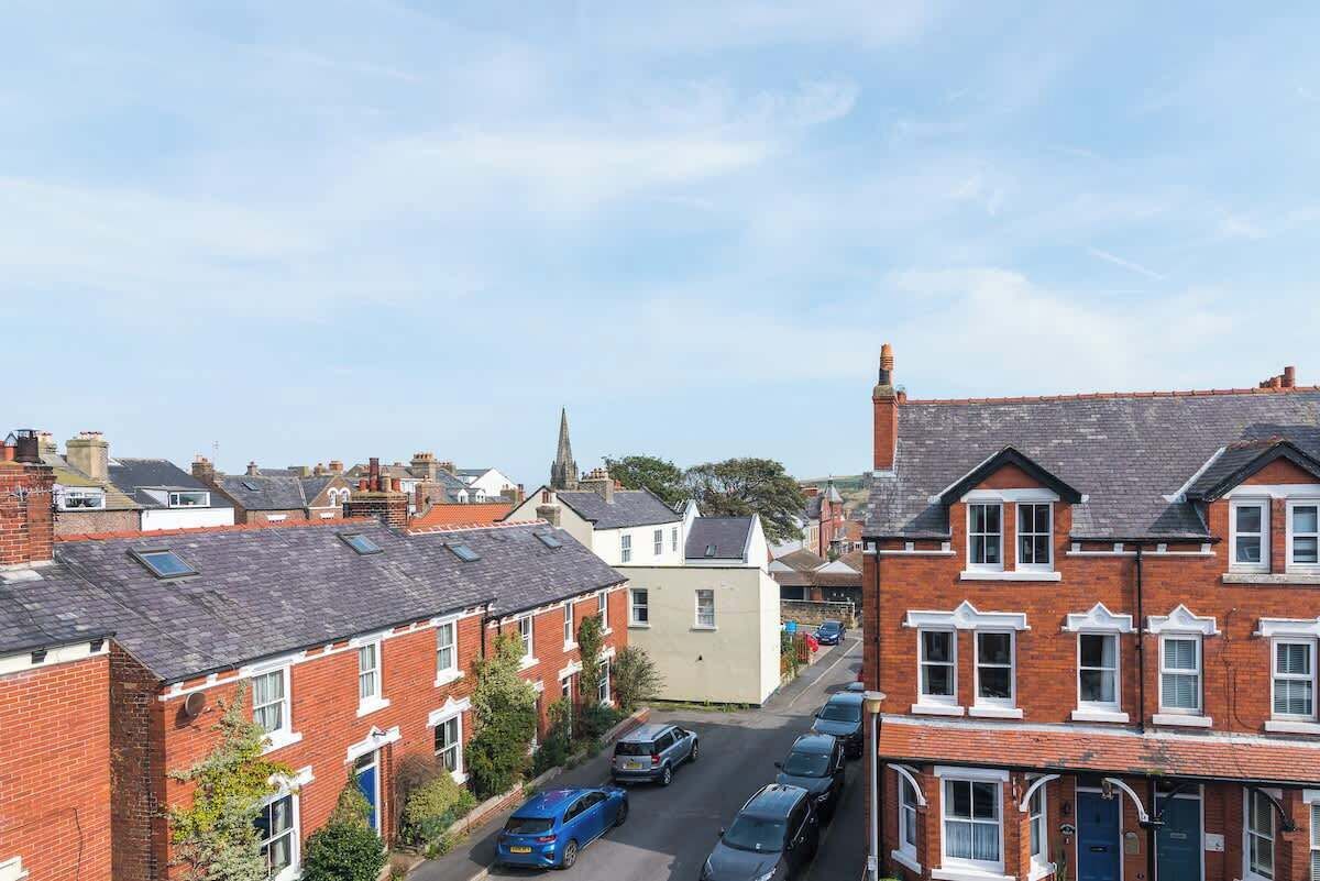 A residential street with terraced houses, parked cars, and a church spire in the distance.