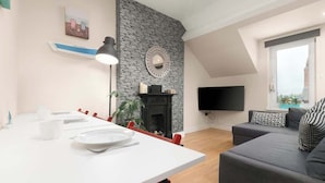 Un salon moderne avec une cheminée, un coin repas avec une table blanche et un canapé gris.
