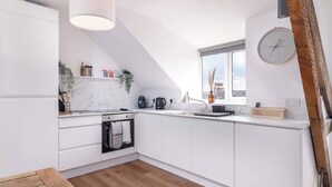 Una cocina moderna con armarios blancos, encimera de mármol y horno empotrado. Hay una ventana que ofrece luz natural y vistas a la ciudad.