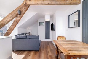 A loft-style room with a wooden staircase, a gray sofa, a wooden dining table, and a city view. - The Snug by the Sea - Central Whitby, Beach Front (West Cliff)