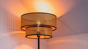 Una habitación moderna con una lámpara de pie alta, una mesita de noche de madera y una silla blanca.