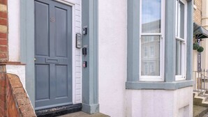 Una puerta gris con una placa de identificación, un marco blanco y una ventana con marco blanco y un toldo negro.