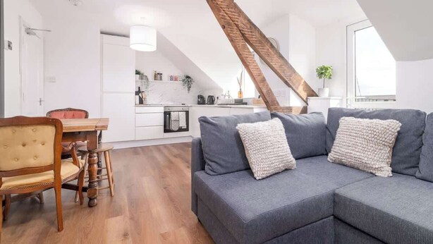 Un loft moderno con vigas de madera a la vista, un sofá gris y un comedor con sillas de madera.