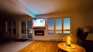 Una sala de estar con chimenea, televisor y vistas al exterior.
