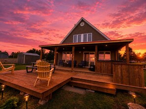 Eine Holzterrasse mit Außenmöbeln, eine überdachte Veranda und ein Haus mit großen Fenstern.