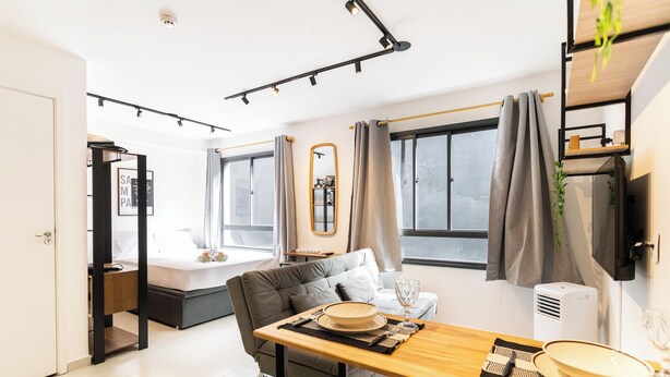 A modern, well-lit room with a dining table set for two, a sofa, and a bed in the background. - Bem Viver Lopes de Oliveira (São Paulo)
