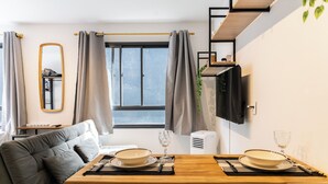 A modern living room with a sofa, a dining table set with plates and glasses, a TV mounted on the wall, and a window with curtains. - Bem Viver Lopes de Oliveira (São Paulo)
