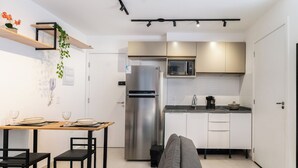 A compact kitchen with a refrigerator, microwave, and a dining area with a table and chairs. - Bem Viver Lopes de Oliveira (São Paulo)