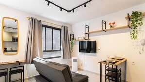 A modern living room with a sofa, a small dining table, a TV, and a window with curtains. - Bem Viver Lopes de Oliveira (São Paulo)
