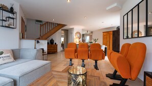 Een moderne woonkamer met een bank, oranje fauteuils, een salontafel en een trap.