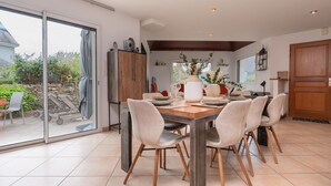 Een eetgedeelte met een tafel voor vier personen, een schuifdeur naar een terras, en een keuken op de achtergrond.