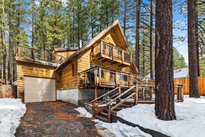 A log cabin with a two-story balcony, a garage, and a snow-covered ground. - Sierra Pines Cabin BBQ, Fireplace, Updated Kitchen (South Lake Tahoe)