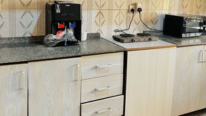 Et køkken med hvide træskabe, en mikroovn, en kaffemaskine og et flisebeklædt backsplash.