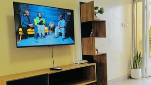 A modern living room with a flat-screen TV mounted on the wall, a wooden entertainment unit below, and a glass coffee table.