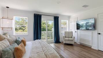 A bedroom with a large bed, a TV, a chair, and a balcony with curtains.