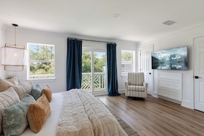 A bedroom with a large bed, a TV, a chair, and a balcony with curtains.