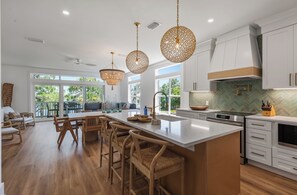 A modern kitchen with a large island, pendant lights, and a view to the outdoor seating area. - Making Memories, Beach, Golf Cart, Pool & Dock (Santa Rosa Beach)