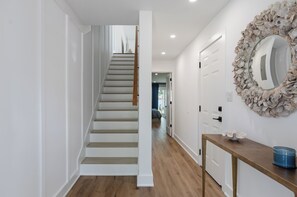 A staircase leading to a second floor, a hallway with a wooden floor, white walls, and a decorative mirror.
