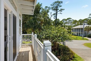 A wooden deck with a white railing, a view of a road, and surrounding greenery.