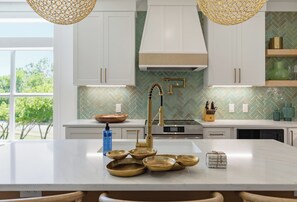 A modern kitchen with white cabinets, a central island with a gold faucet, and a green herringbone backsplash. - Making Memories, Beach, Golf Cart, Pool & Dock (Santa Rosa Beach)