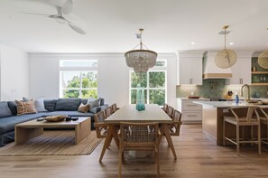 A modern living room with a dining area, a kitchen with a herringbone backsplash, and a large window.