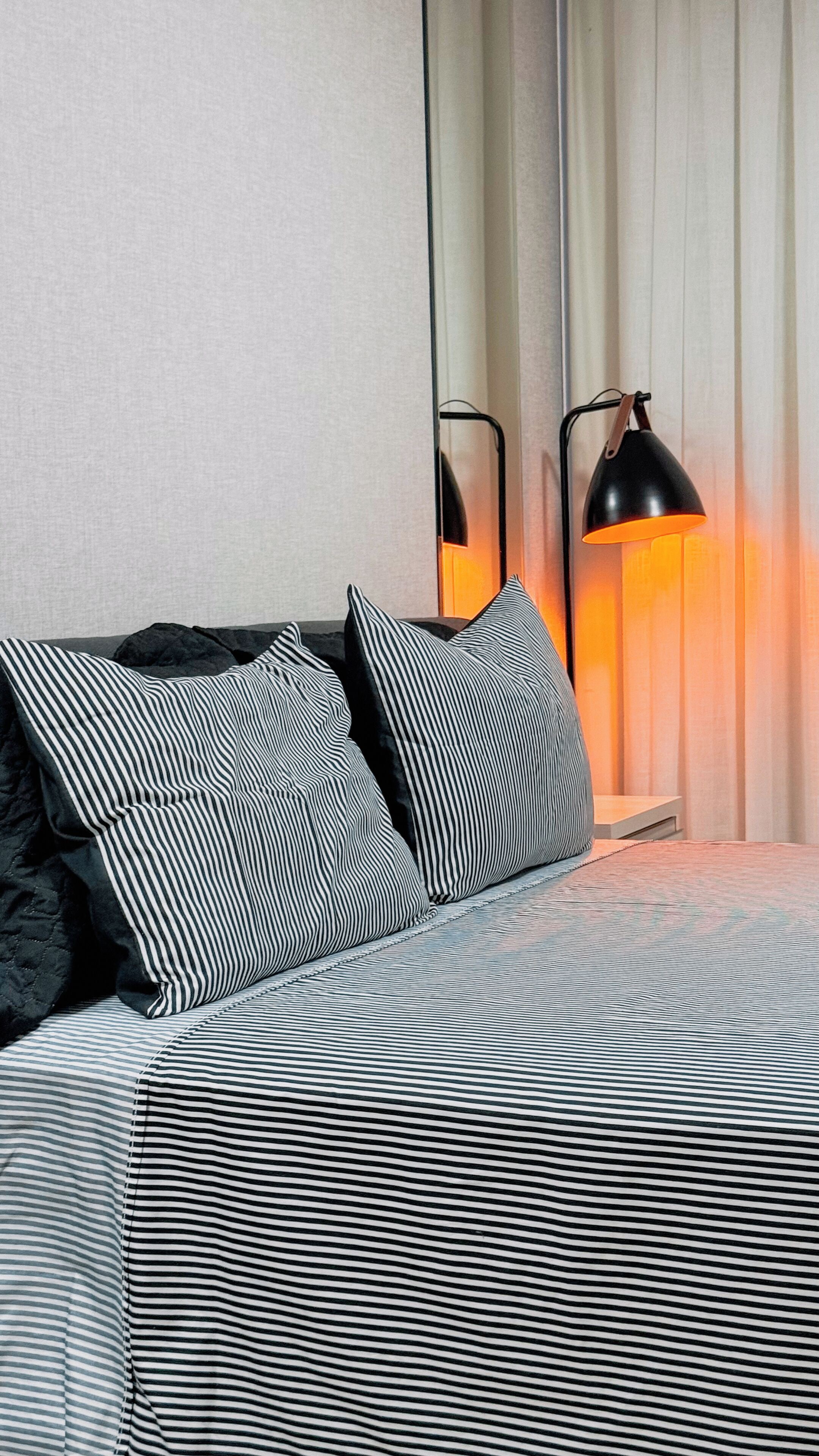 A hotel room with a bed featuring striped bedding, a black lamp, and a curtain.