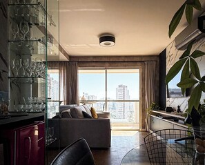Ein modernes Wohnzimmer mit einer Couch, einem Esstisch und einer Glasvitrine mit Weingläsern.