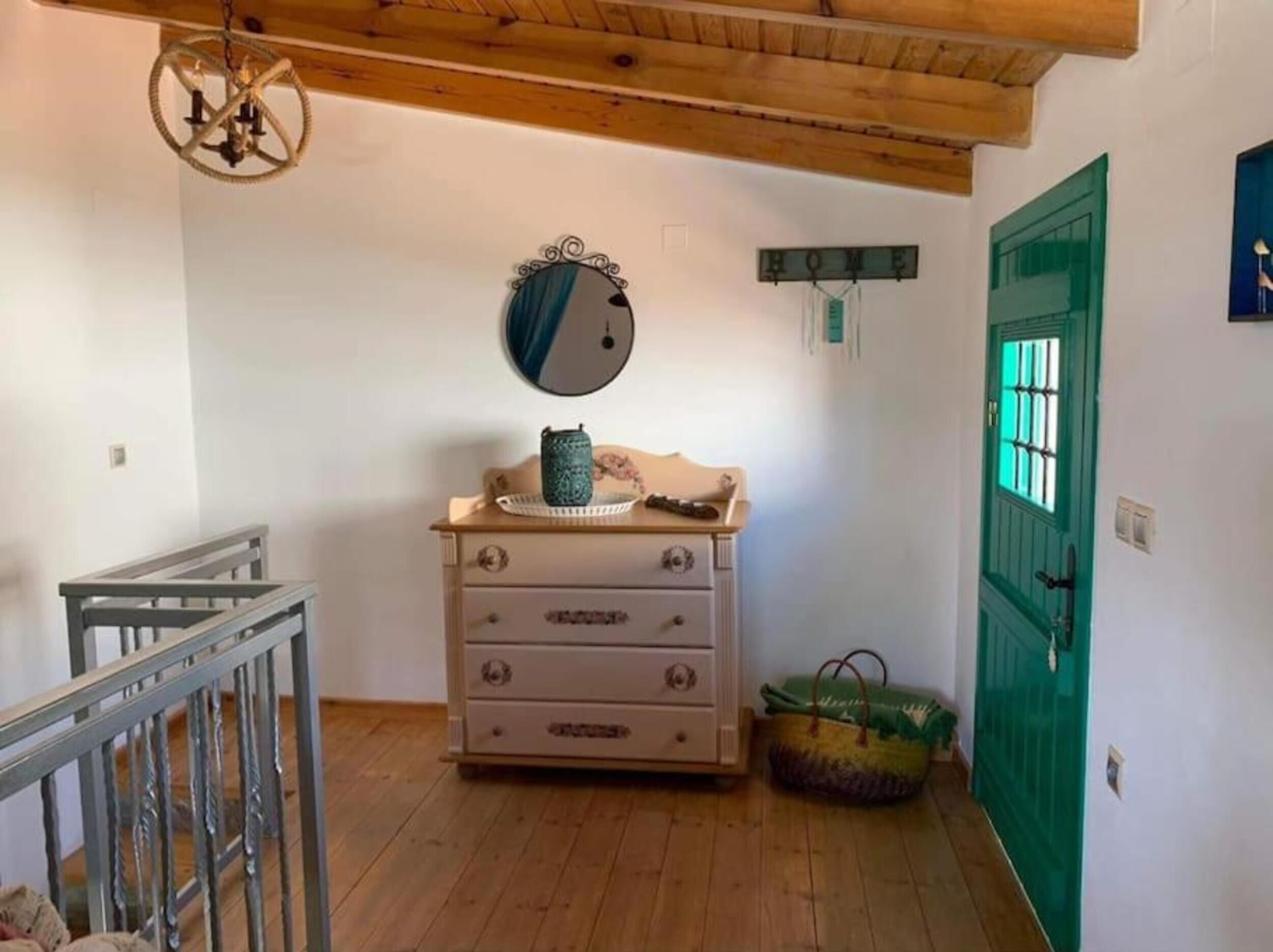 A room with a wooden ceiling, a green door, a dresser with drawers, a mirror, and a hanging light fixture.