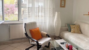 A living room with a white sofa, an orange chair, a glass coffee table, a radiator, and a window with sheer curtains. - Apartment in a quiet street (Schiltigheim)