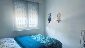 A bedroom with a bed, a window with blinds, and two dreamcatchers on the wall. - Apartment in a quiet street (Schiltigheim)