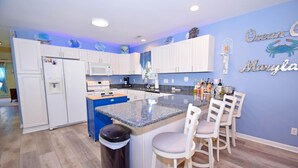 A modern kitchen with white cabinets, a granite countertop, and a bar area with white stools. - Montego Bay-colonial Drive 13339 3 Bedroom Home (Ocean City)