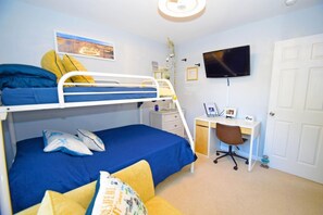 Une chambre avec un lit superposé, un bureau et une chaise, une télévision et une porte.
