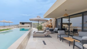 Uma área à beira da piscina com espreguiçadeiras, uma parede de pedra e vista para o mar.