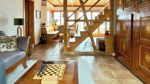 Ein geräumiger Wohnbereich mit einer Holztreppe, einem Sofa, einem Schachbrett und einer Vitrine mit Dekorationen.