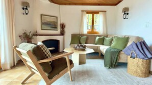 Ein gemütliches Wohnzimmer mit Holzbalkendecke, einer Sofagarnitur, einem Sessel, einem Couchtisch und einem Korbwäschesessel.