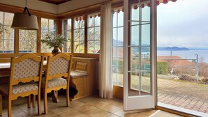 Ein Essbereich mit Holzkufen und einem Tisch, große Fenster mit Blick ins Freie und eine Glastür zum Garten.