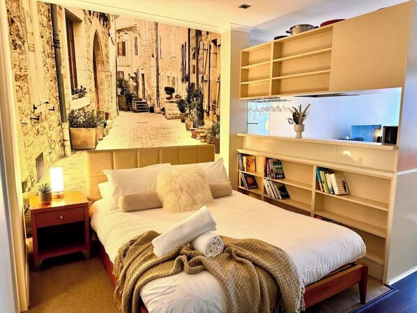 Une chambre à coucher comprenant un lit, des tables de chevet, une bibliothèque et un mur orné d’une fresque.
