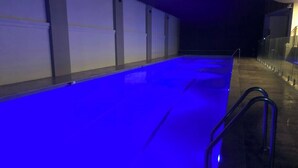Una piscina con iluminación azul, rodeada de muros y una barrera de cristal.