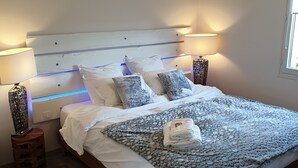 Siististi pedattu sänky, jossa on kuviollinen peitto, kaksi yöpöytävalaisinta ja suuri kattovalaisin.