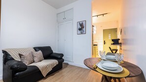 A modern living room with a black leather sofa, a dining table with glassware, and a white door in the background. - StayHome 1min da Praia | São Vicente SP | Família ou Casal (São Vicente)