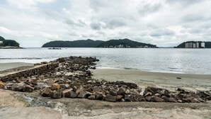 A rocky shoreline with a stone wall and calm water. - StayHome 1min da Praia | São Vicente SP | Família ou Casal (São Vicente)