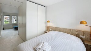 A hotel room with a bed, a wardrobe, a bedside table with a lamp, and a view of the outside. - Casa Vento -  Koksijde (Koksijde)