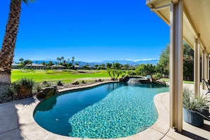 A swimming pool with a clear blue water surface, surrounded by a landscaped garden with palm trees and a view of a golf course and mountains in the distance. - 4 Bedroom Private Pool Home in Mira Vista (Rancho Mirage)