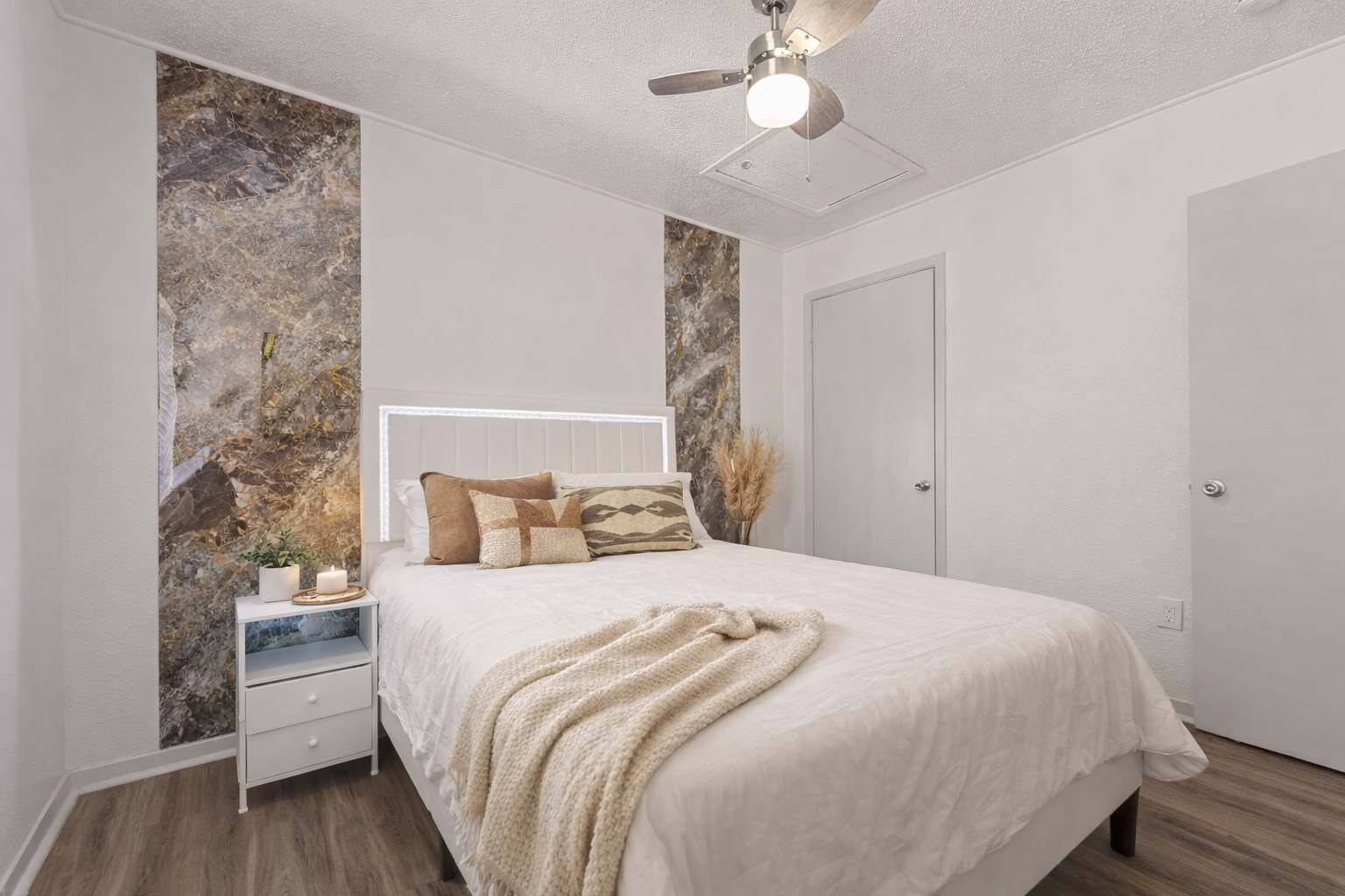 A bedroom with a bed, nightstand, bedside table, and a ceiling fan.