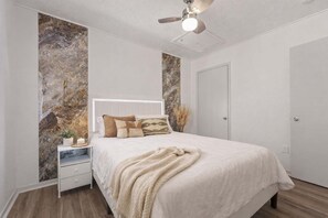 A bedroom with a bed, nightstand, bedside table, and a ceiling fan. - Entertainment District Escape • 2BR + Parking (Arlington)
