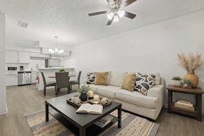 A modern living room with a sofa, coffee table, and a dining area in the background. - 2BR • 8 Min Walk to AT&T Stadium • Free Parking (Arlington)